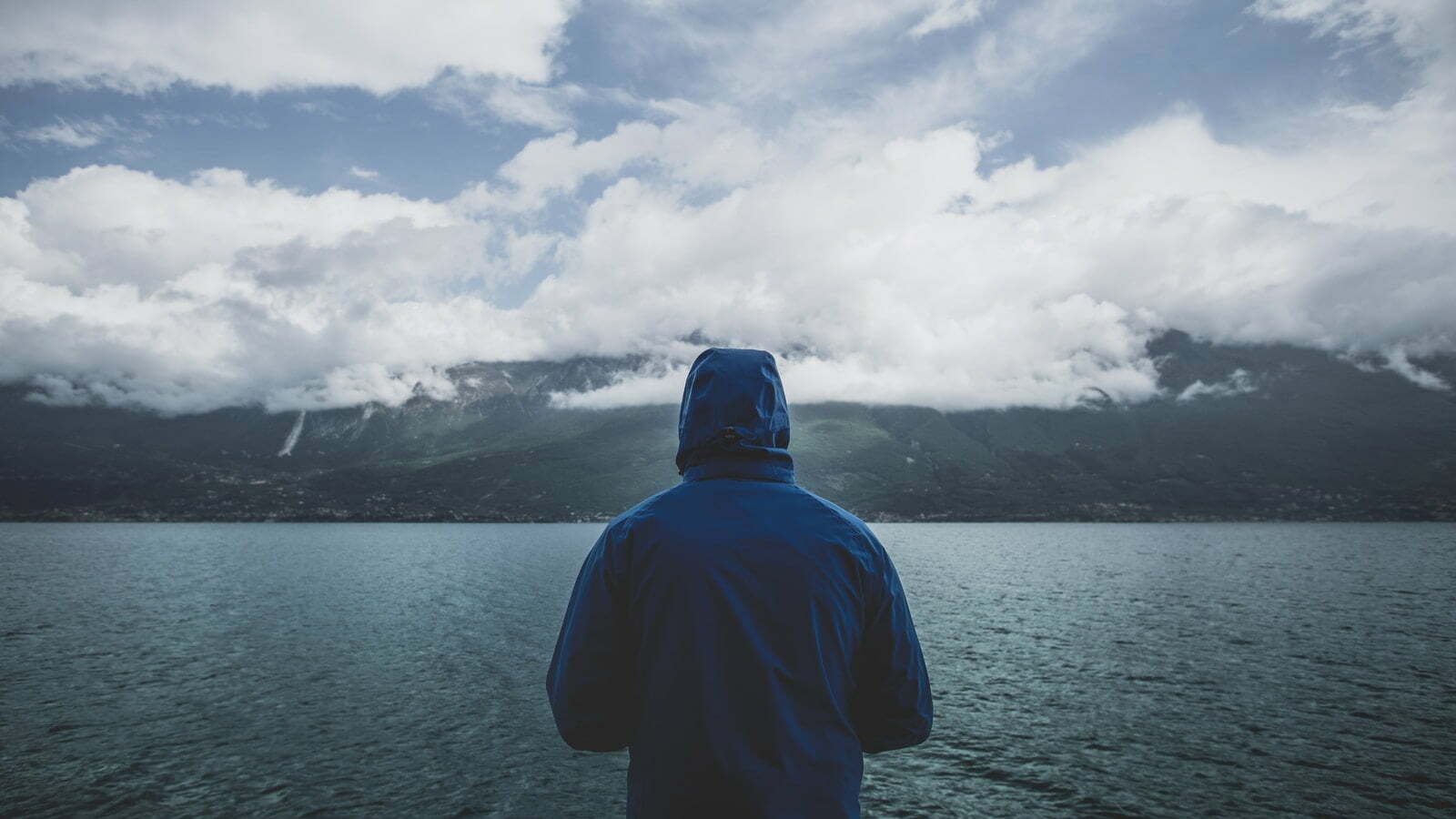 person wearing blue hoodie standing infront of body of water